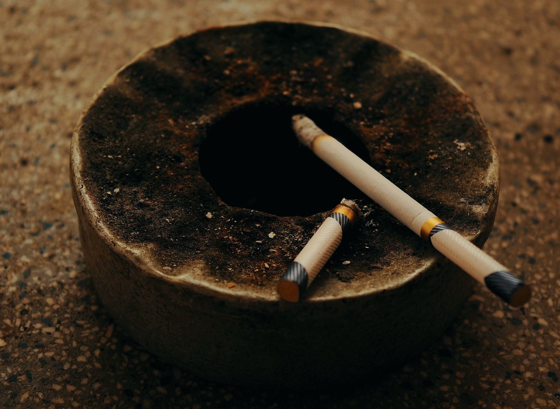 old ashtray with burnt cigarettes on rough surface